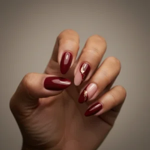 Imagem close-up de uma mão com unhas compridas esmaltadas na cor vinho. As unhas dos dedos médio e anelar estão decoradas com as cores vinho, rosa e dourado.
